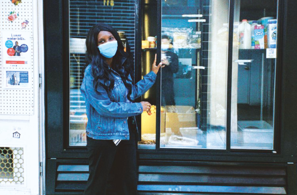 Wearing a medical face mask, Desuana Dubose holds open the glass door of a commercial refrigerator at the People’s Fridge on 52nd.
